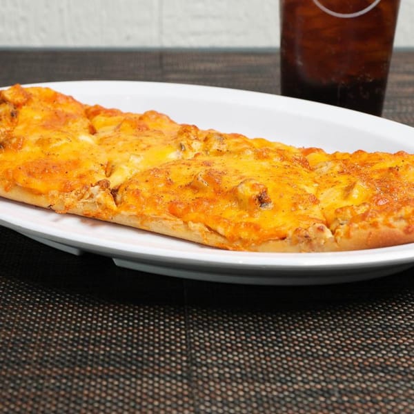 A long, oval flatbread pizza covered in melted cheese and spices, with a drink in the background.