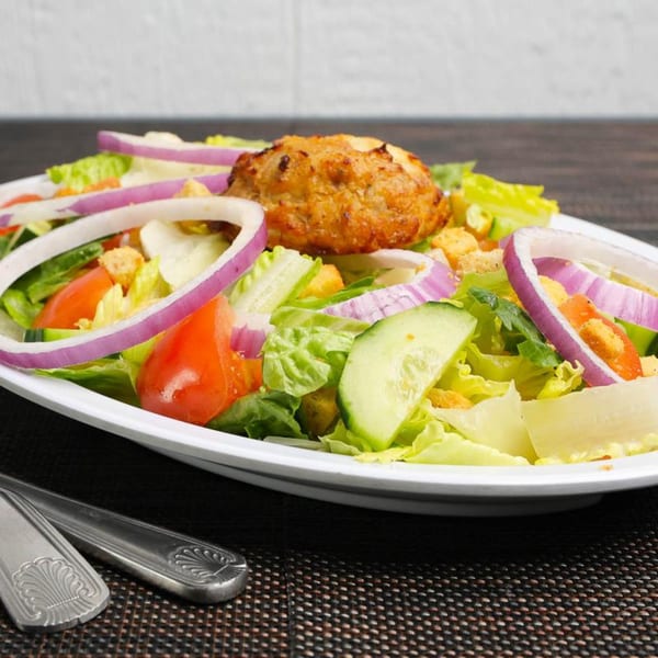 Fresh garden salad with lettuce, tomatoes, red onions, cucumbers, croutons, and a crab cake.