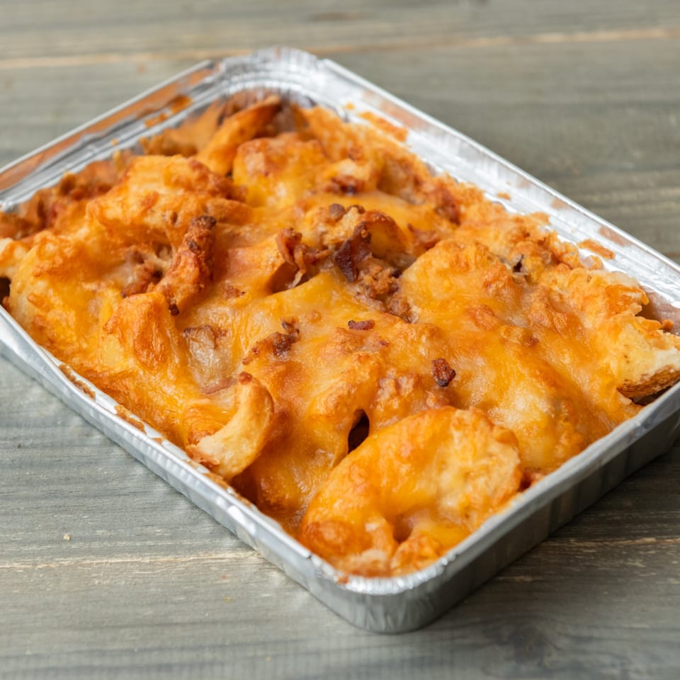 Cheesy baked pasta in a rectangular aluminum foil container on a wooden surface.